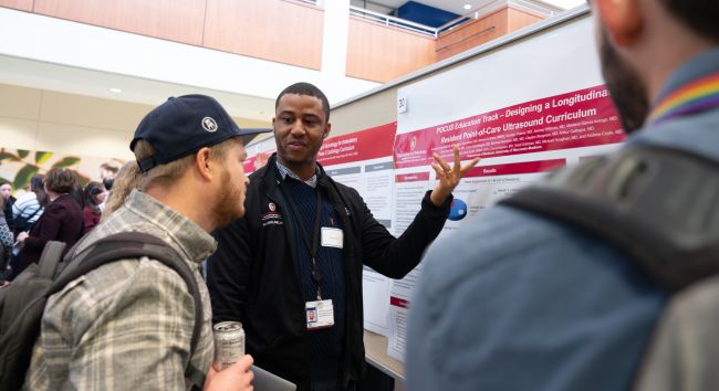 Internal medicine resident Akinwale Iyeku, MD, MS, PG-2, walks an onlooker through his poster presentation.