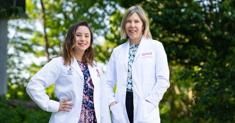 Lydia Buzzard and Sarah Ahrens stand outside wearing their white coats