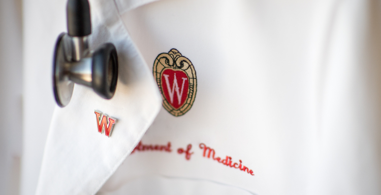 Physician's white coat embroidered with UW logo and the words Department of Medicine, with a W red enamel pin and stethoscope.