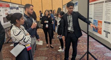 An internal medicine resident discusses his conference poster with onlookers.
