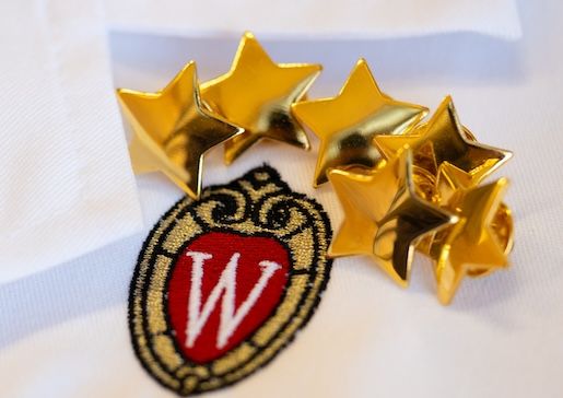 Closeup photo of metal gold stars sitting on top of white coat with embroidered University of Wisconsin crest